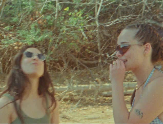 Two women eat food in their bathing suits on the sand