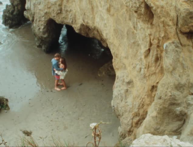 Romantic couple dancing together next to a cave in the sand on the beach