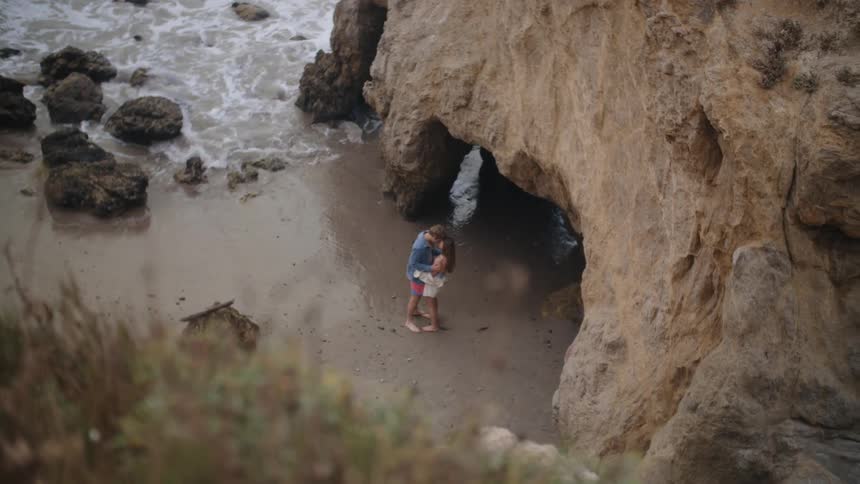 A man and woman hug by the sea cave