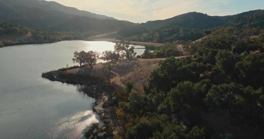 A calm lake nestled among rolling hills reflecting the golden light of the setting sun