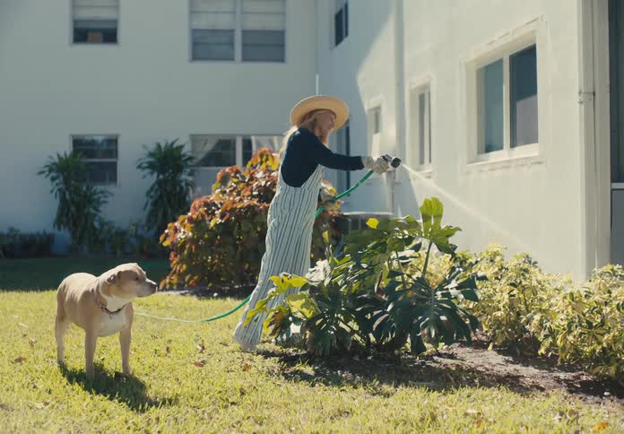 Woman watering plants in a garden and a dog next to her