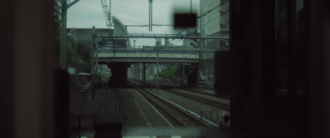 A view from the front of a train moving along railway tracks passing under multiple overpasses and surrounded by urban infrastructure