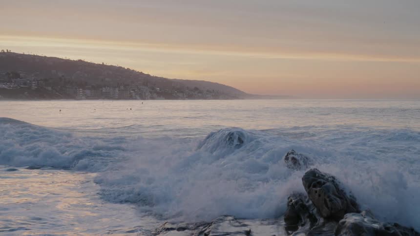 Waves crash against a rocky shore at sunset