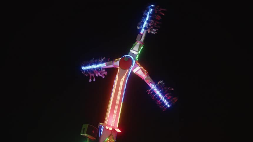 Upward view of an operating ride with people at an amusement park at night