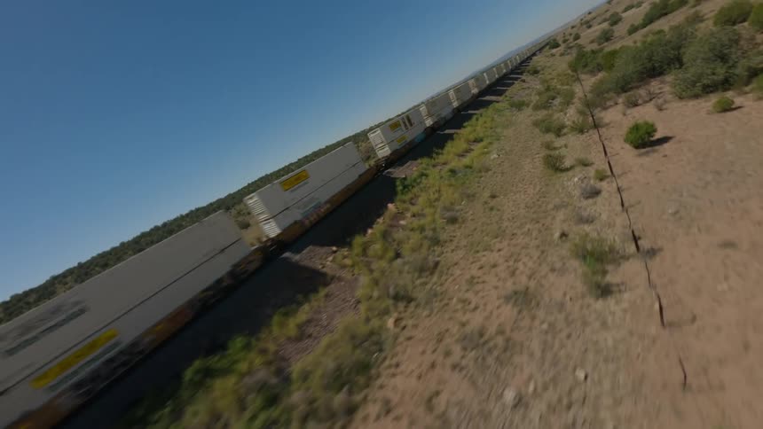 An aerial view shows a long freight train traveling through a dry sparsely vegetated landscape