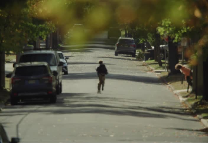 Boys riding down middle of street on skateboards through a neighborhood