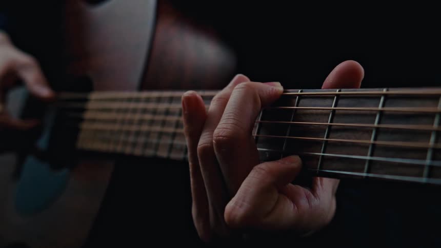 A guitarist wearing a black sweater strums an acoustic guitar