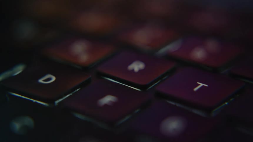 A closeup of a laptop keyboard illuminated by a dim light