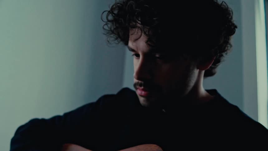 Man with a mustache and a black sweater strums a acoustic guitar