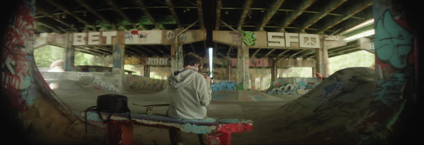 A teenager is skateboarding in a skate park under a overpass