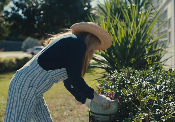 Woman with gloves and a hat placing a potted plant in a garden