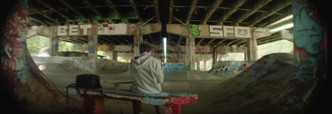 Boy with a camera filming another teenager doing skateboarding tricks on a track below an overpass