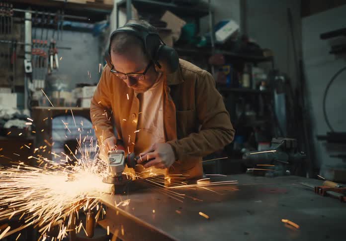 Man with glasses and protective headphones melting iron with sparks