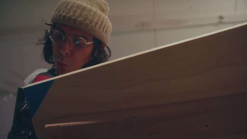 Carpenter with cap on head pouting and working with screwdriver on a sheet of wood