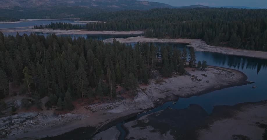 A large lake winds its way through a forested landscape at dusk with the water reflecting the darkening sky