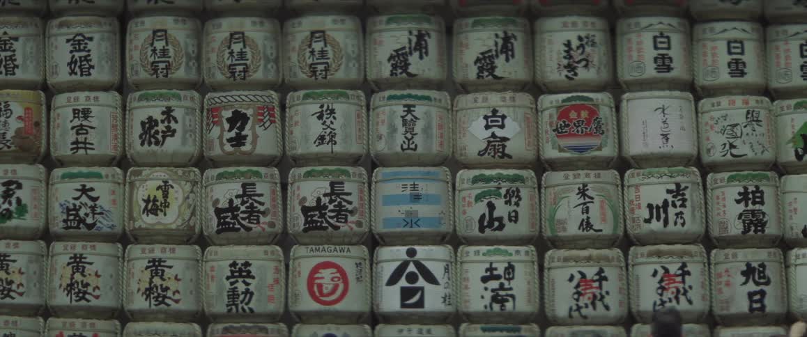 People walking in Tokyo and in the background white casks with Japanese writings