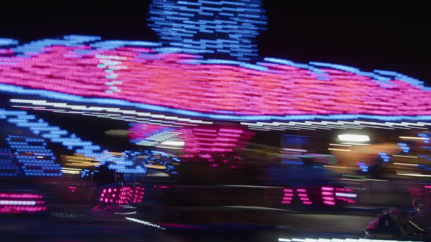 People on moving and operating rides at an illuminated amusement park at night