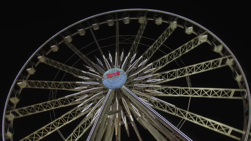A large ferris wheel with illuminated cabins rotates against a dark night sky