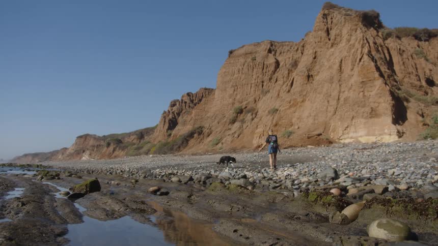 A woman and her dog are hiking by a mountain