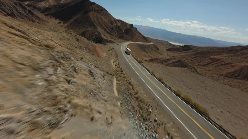 Aerial view of a bus traveling along a paved road surrounded by mountains with arid vegetation