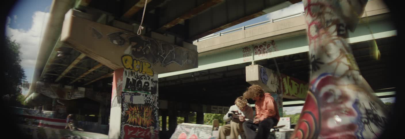 Two teenagers sitting below an overpass bench talking