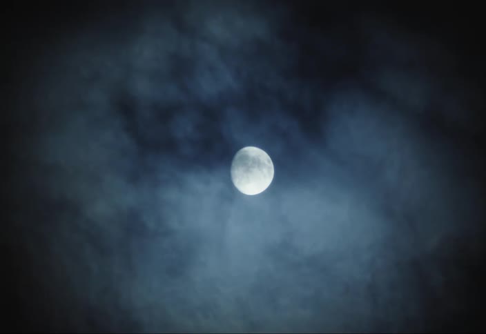 A full moon shines brightly through a layer of thin wispy clouds in the night sky