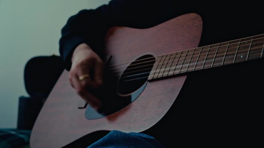 Man with a mustache and a black sweater strums the strings of an acoustic guitar