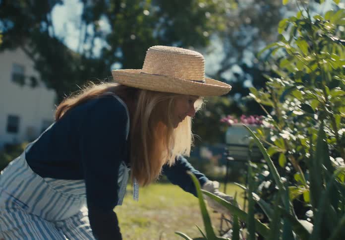 Woman wearing a sun hat is crouched down with gloves gardening