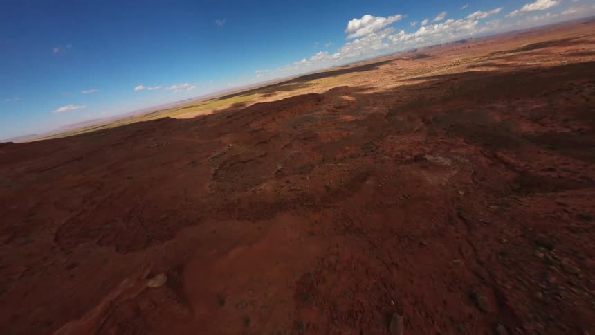An aerial view of a vast arid desert landscape with reddishbrown terrain and sparse vegetation under a clear blue sky with scattered clouds