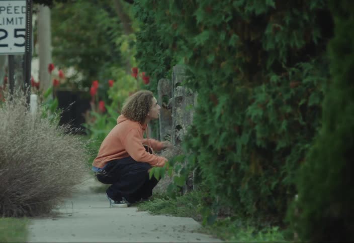 Two kids with a skateboard on their backs and next to a person looking through the fence