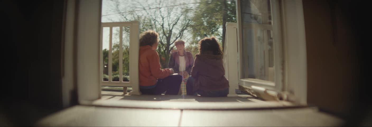 Two friends sitting next to a girl in the entrance of a house
