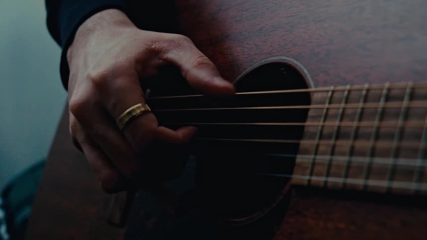 Man wearing a gold ring strumming a dark acoustic guitar