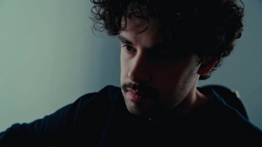 Man with a mustache and a black sweater plays an acoustic guitar
