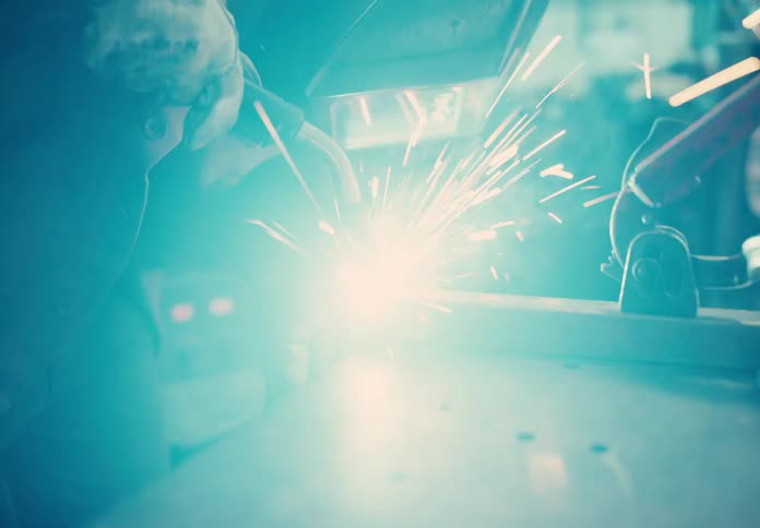 A closeup view of a welders torch at work sparks flying and casting a bright glow on the metal being joined