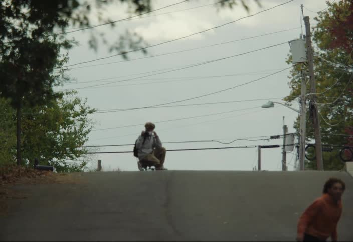 Boy skateboarding down the street and another taking pictures