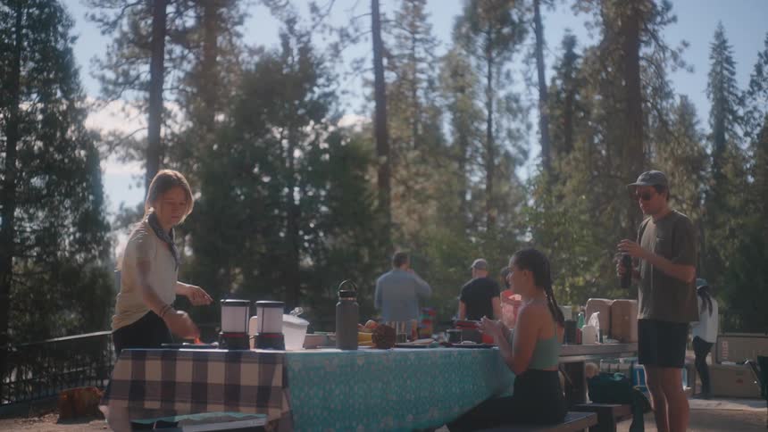 Group of people eating and drinking at outdoor tables with trees in the background