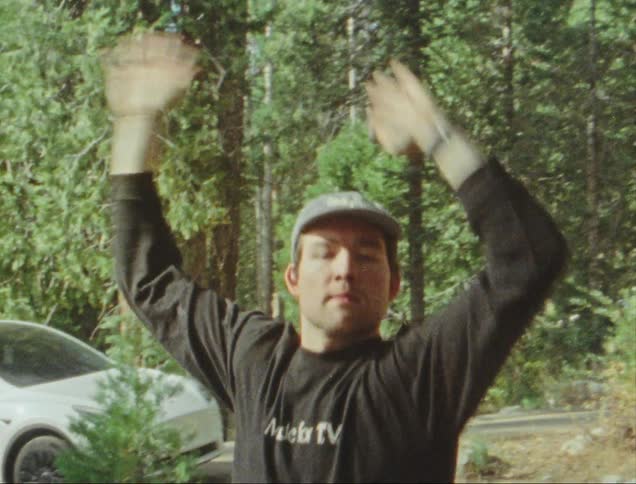 Man outdoors surrounded by trees with arms up dancing happily