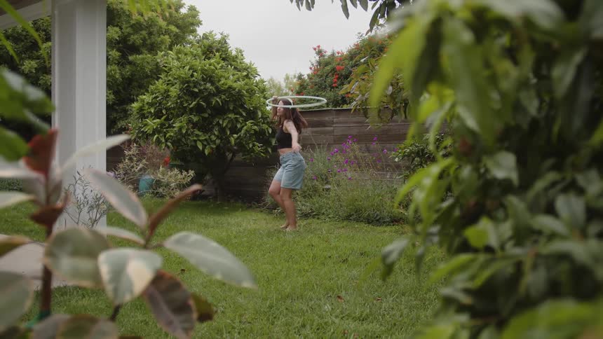 Woman in a backyard with headphones dancing outdoors with a hula hoop on her body