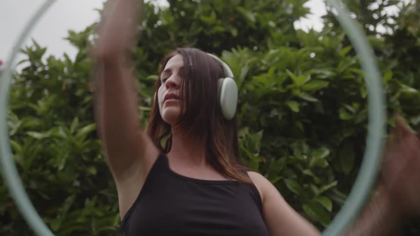 Woman with headphones dancing in a garden with a hula hoop