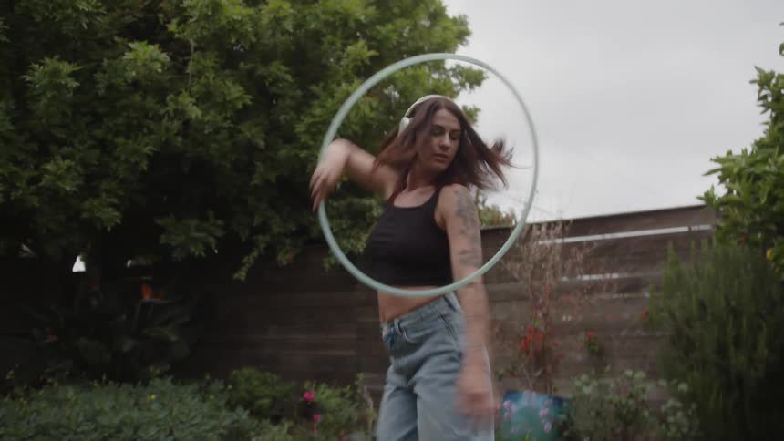 Woman with headphones dancing with a hula hoop in a backyard