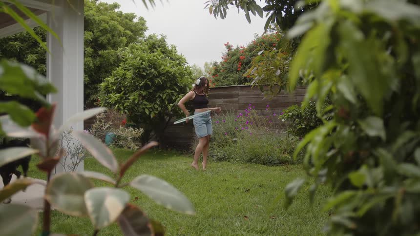 Woman in a garden spinning her body with a hula hoop and a dog running beside her