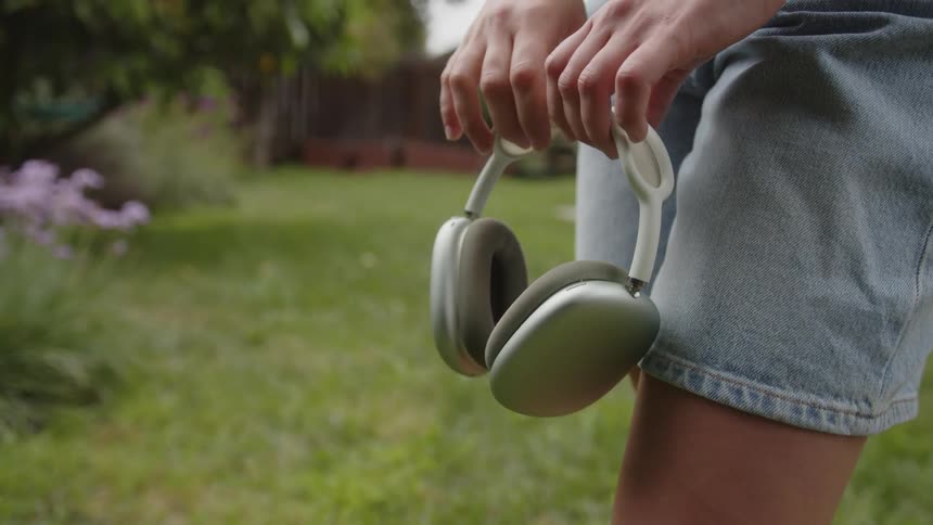 A girl wearing shorts holds a pair of silver headphones in their hand