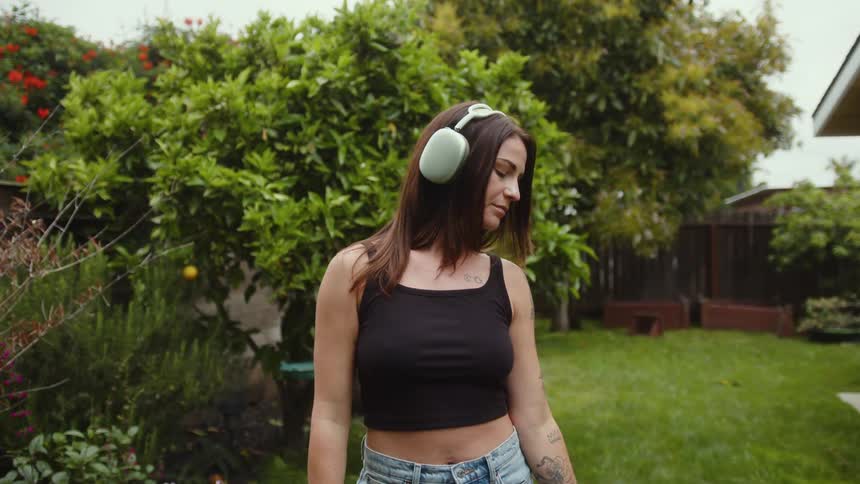 Woman with headphones stands in a grassy yard and holds a hula hoop
