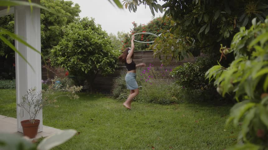 Female wearing headphones twirling with a hula hoop in the backyard