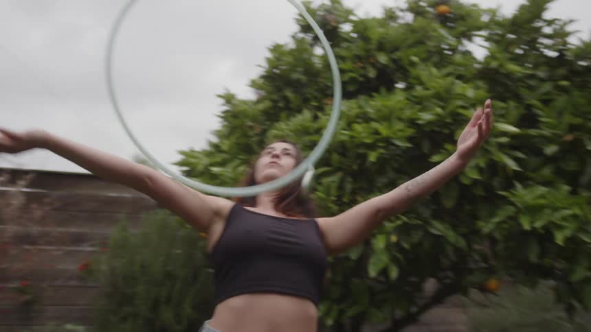 A woman is hula hooping outdoors while wearing headphones