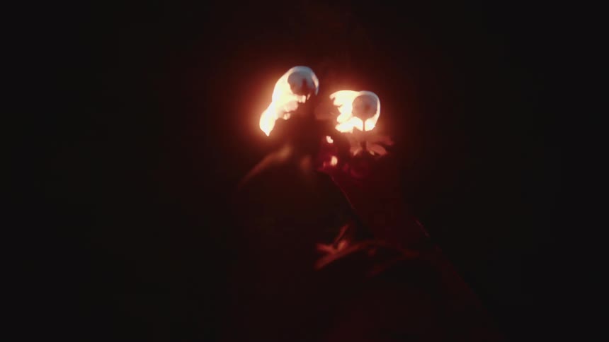 Woman turns in place while holding two small burning torches above her head