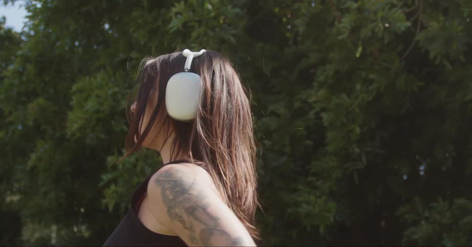 Woman dancing outdoors next to a tree with a hula hoop and headphones