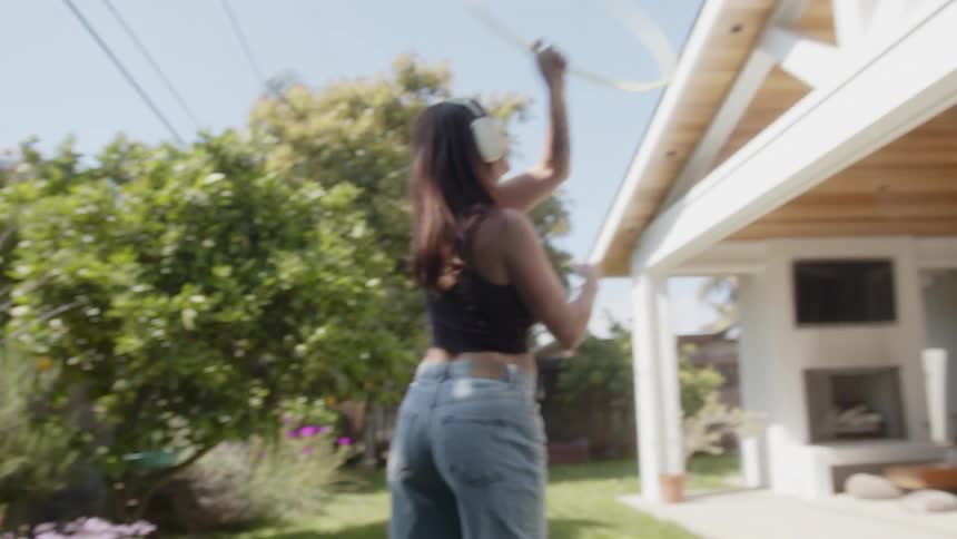 A woman is hula hooping outdoors while wearing headphones with trees visible in the background