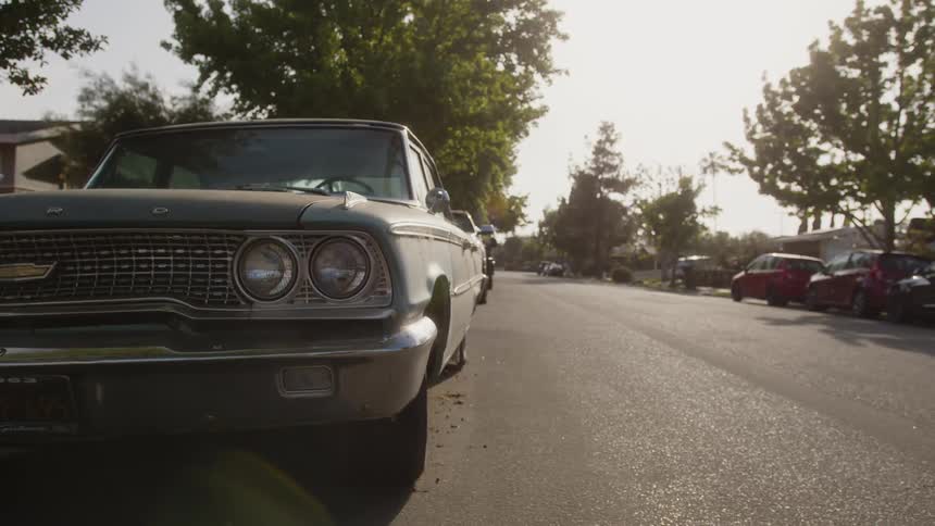 A vintage car is parked on a residential street with the afternoon sun casting a warm light on its front end