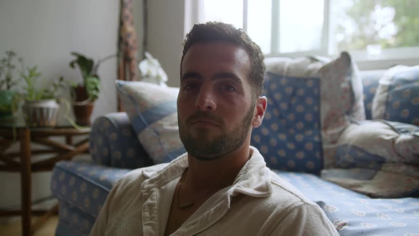 A handsome bearded man sits on the living room floor looking at the camera